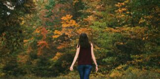 woman in brown sleeveless dress and blue jeans standing on gray path road